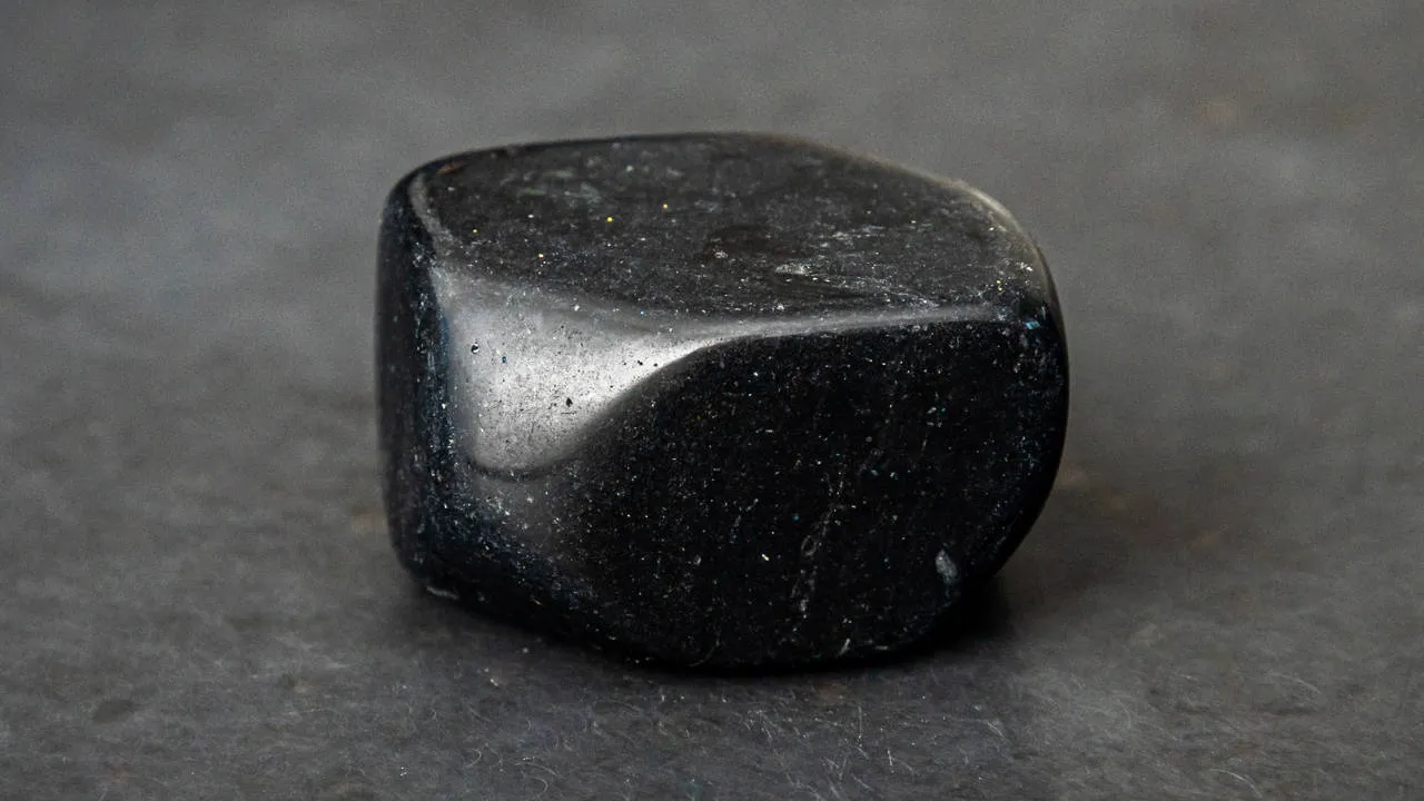 Tumbled black agate energy stone with a natural matte finish and subtle crystalline textures.