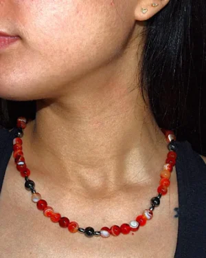 Collar de cuentas de ágata roja y hematita oscura, destacando sobre el cuello de una persona. La energía vibrante del ágata se combina con la fuerza protectora del hematita para crear una joya única.