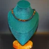 Handmade beaded energy necklace featuring brown tiger's eye and black volcanic lava stones displayed on a teal velvet jewelry bust.