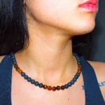 Close-up of a woman wearing an elegant handmade Guaca-inc necklace crafted with genuine Tiger's Eye and porous black volcanic lava stones. Showcasing natural elements and stainless steel details from the Florida online store.