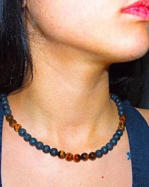 Close-up of a woman wearing an elegant handmade Guaca-inc necklace crafted with genuine Tiger's Eye and porous black volcanic lava stones. Showcasing natural elements and stainless steel details from the Florida online store.