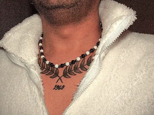 Man with a chest tattoo wearing a beaded necklace featuring white agate and dark hematite stones, paired with a cozy white fleece jacket.