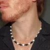 Close-up profile of a young man with a red beard wearing a black open-collar shirt and a handcrafted white agate and dark hematite beaded energy necklace. | Guaca-inc