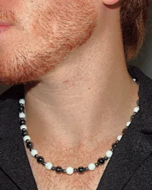 Close-up profile of a young man with a red beard wearing a black open-collar shirt and a handcrafted white agate and dark hematite beaded energy necklace. | Guaca-inc