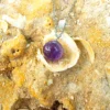 Colgante de cristal de amatista sobre fondo de arena de playa con conchas naturales.