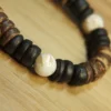 Macro close-up of a polished white Trochus shell bead surrounded by matte black and textured brown coconut shell discs.