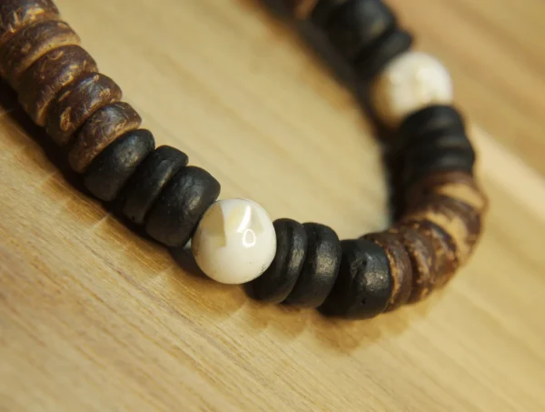 Macro close-up of a polished white Trochus shell bead surrounded by matte black and textured brown coconut shell discs.