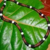 Handmade necklace crafted with natural coconut wood beads and white sea shells, displayed on tropical leaves.