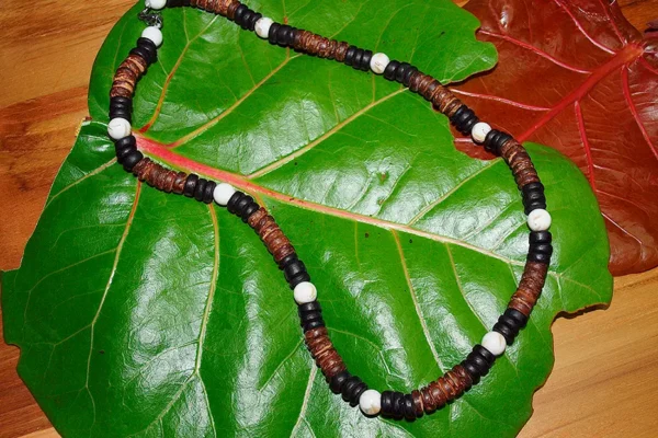 Handmade necklace crafted with natural coconut wood beads and white sea shells, displayed on tropical leaves.