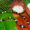 Handmade necklace featuring authentic Queen Conch shell beads and rustic coconut wood spacers, displayed on lush tropical leaves with raw materials.