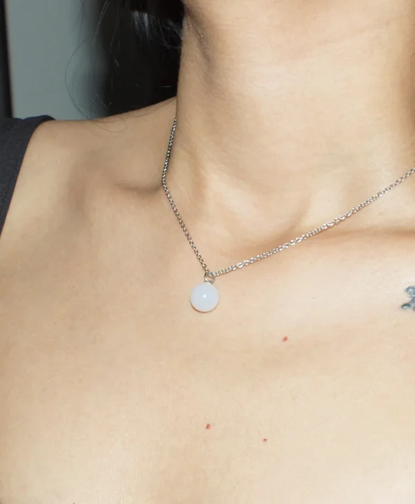 A close-up lifestyle shot of a woman wearing a spherical White Agate crystal necklace; known as one of the best crystal necklaces for anxiety and stress.