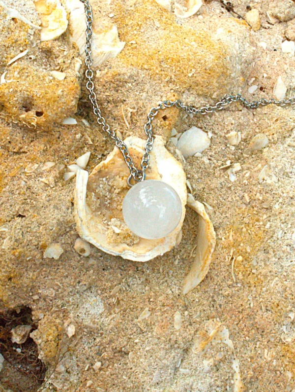 White Quartz sphere pendant necklace on beach sand and sea shells for energy purification.