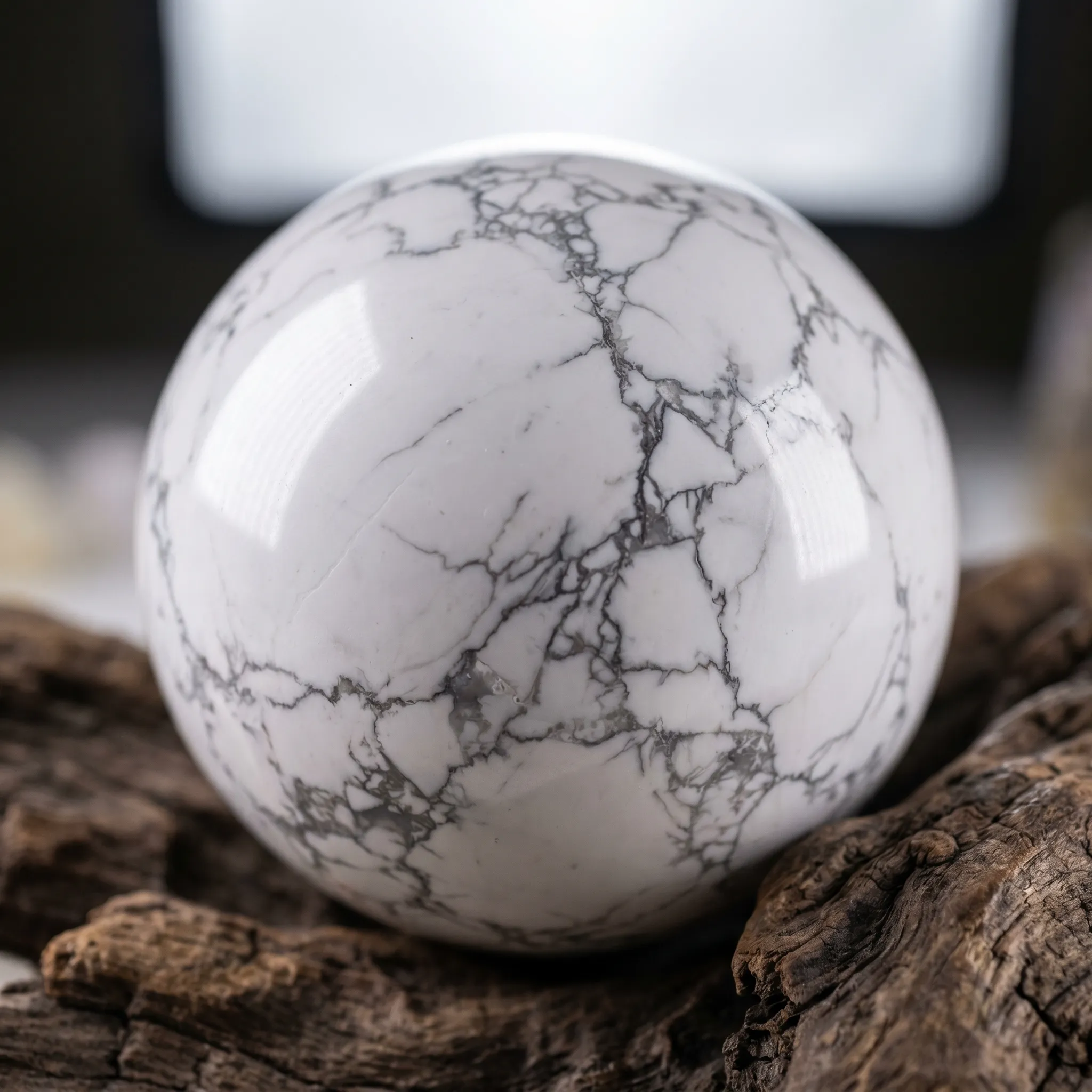 Perfect polished white howlite stone sphere with gray veins resting on a rustic wood base.
