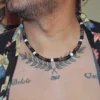 Close-up of a man with a chest tattoo wearing an open black floral tropical shirt and a Queen Conch and coconut shell beaded choker necklace.