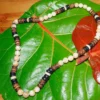 Flat lay product photograph of a handcrafted Trochus shell and coconut shell beaded necklace displayed open on a large green leaf.